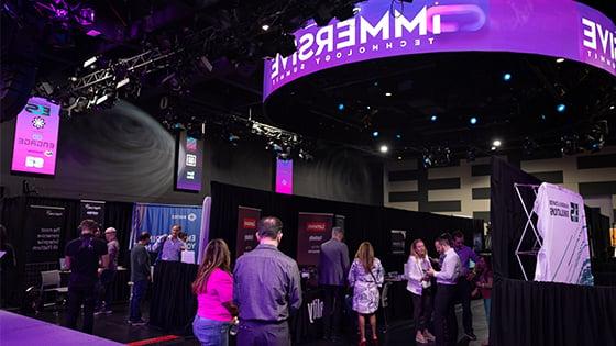 A large room with lots of booths set up, each from a different technology company. People in business-casual clothing are walking around 和 socializing.